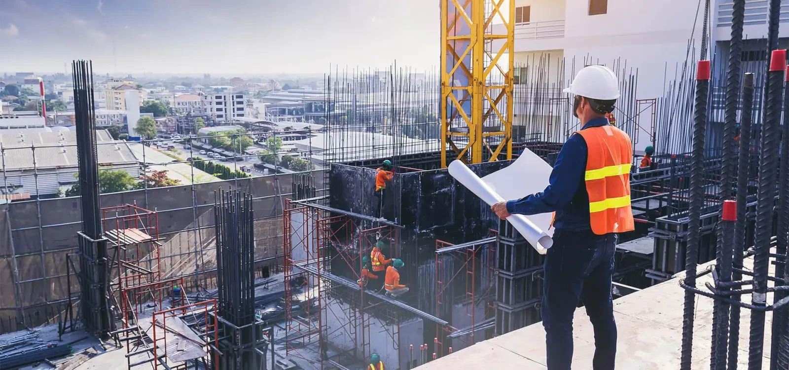 Engineer in a hard hat holding drawings above a high-rise construction site