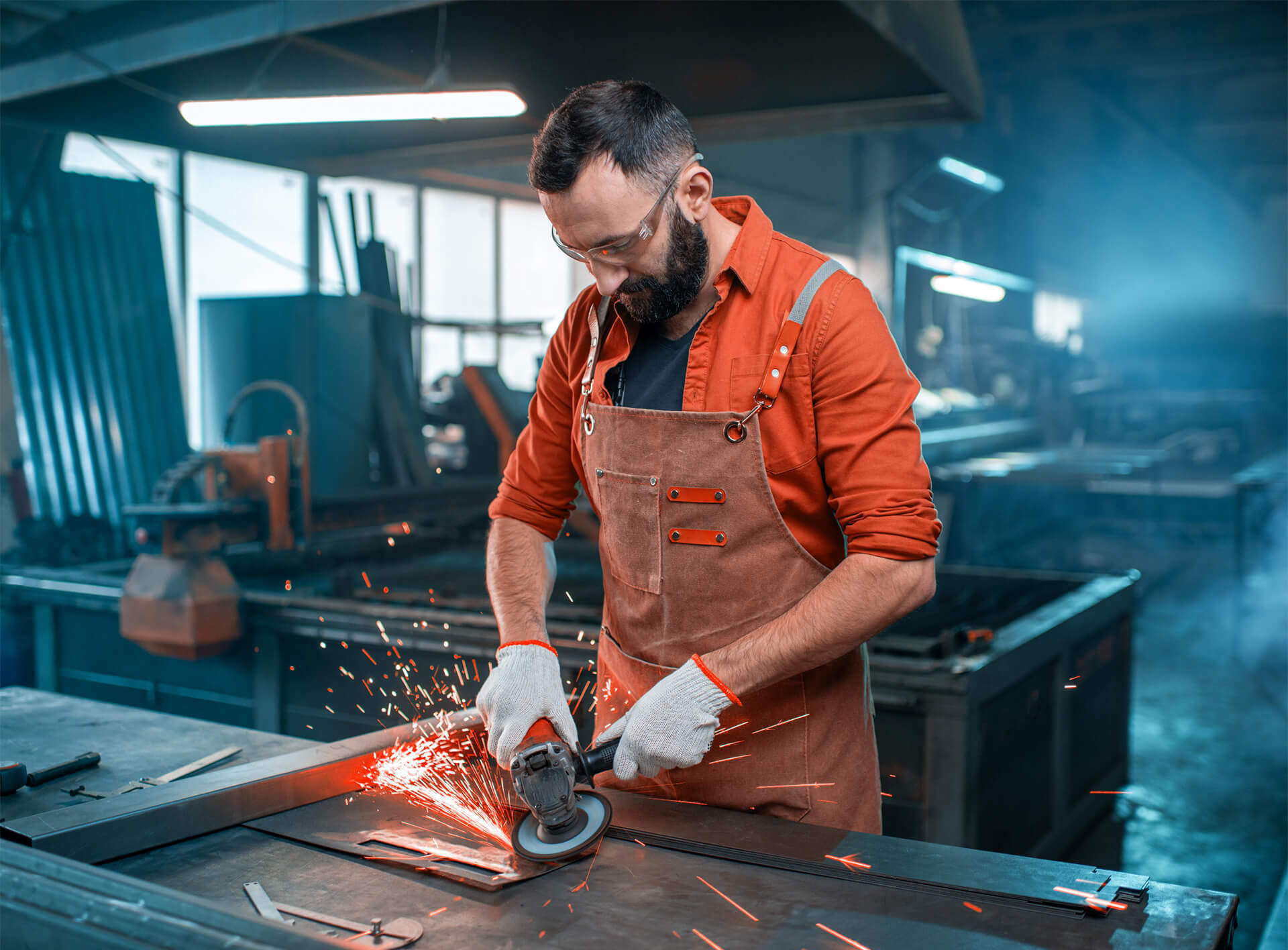 Metalworker in an apron grinding a steel sheet at a workbench
